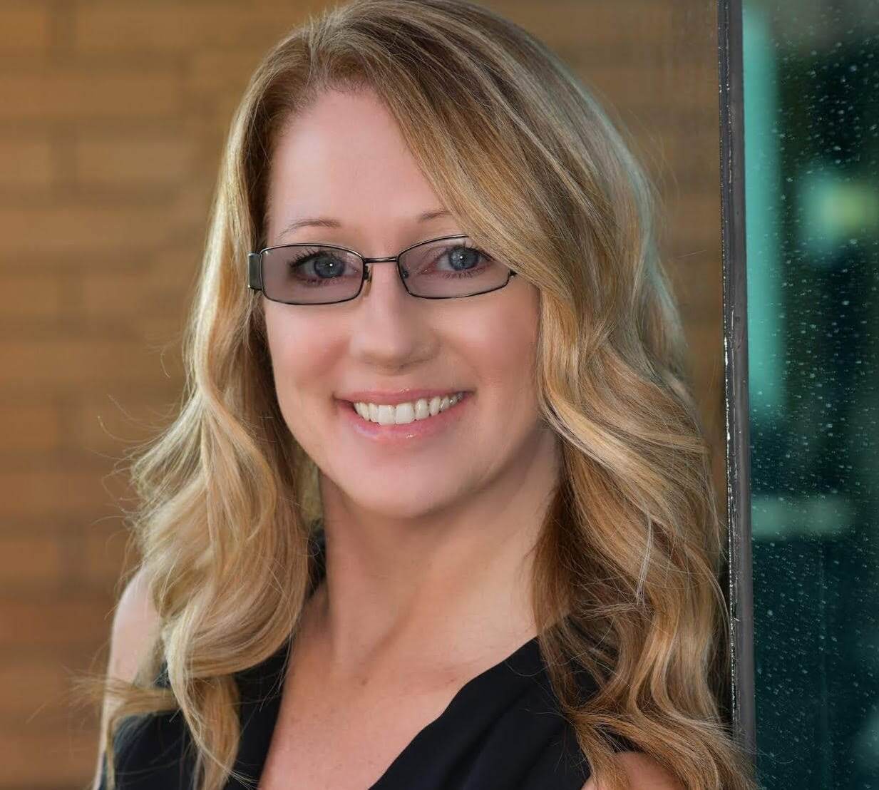 Meet Laura Myers! An interview with Meet Laura Myers, Top Solo Agent. Laura has long blonde hair, is wearing glasses and a dark shirt, and is facing forward while smiling.