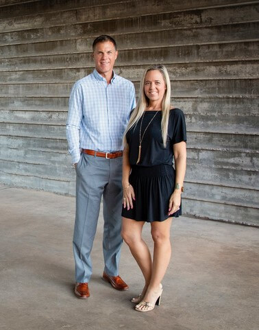 Meet David and Shannon Johnson! An interview with David and Shannon Johnson. David is Co-Chairperson of the Growth Committee on the Keller Williams Arizona Realty Agent Leadership Council (ALC) for 2022. Shannon is Co-Chairperson of the Culture Committee on the Keller Williams Arizona Realty Agent Leadership Council (ALC) for 2022. David has dark hair, wearing gray pants and light blue shirt, facing forward and smiling; Shannon has long blonde hair, wearing a black short dress, and is standing next to David, facing forward and smiling.