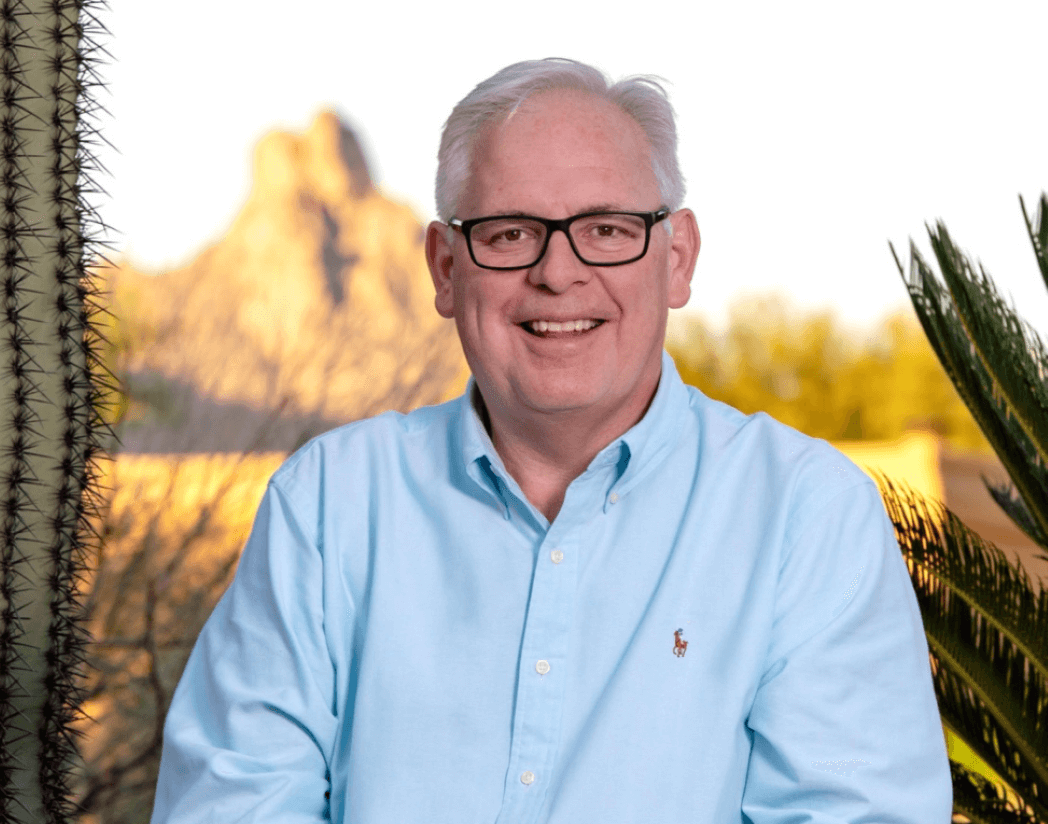 Meet Ted Dudine! An interview with Ted Dudine, REALTOR® who focuses on “Selling Sonoran Sunsets with Hoosier Hospitality®” at Keller Williams Arizona Realty. Ted is smiling, wearing a light blue shirt, has eyeglasses, and is facing forward in front of the background image of Pinnacle Peak. 
