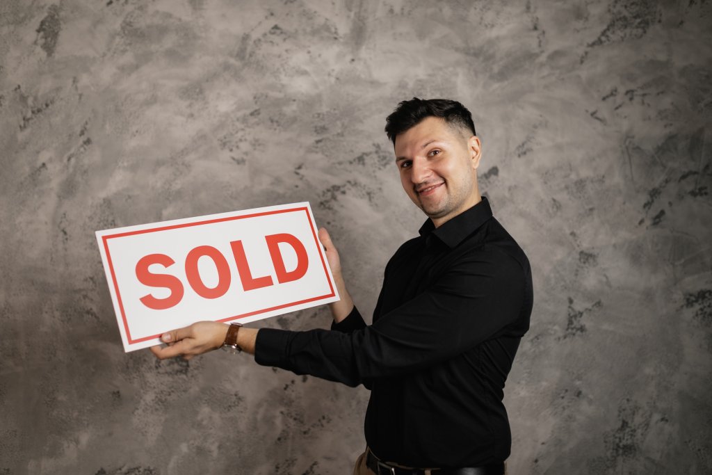 Man wearing black shirt, smiling, holding SOLD sign, happy that his real estate business highlights his Value Proposition to clients